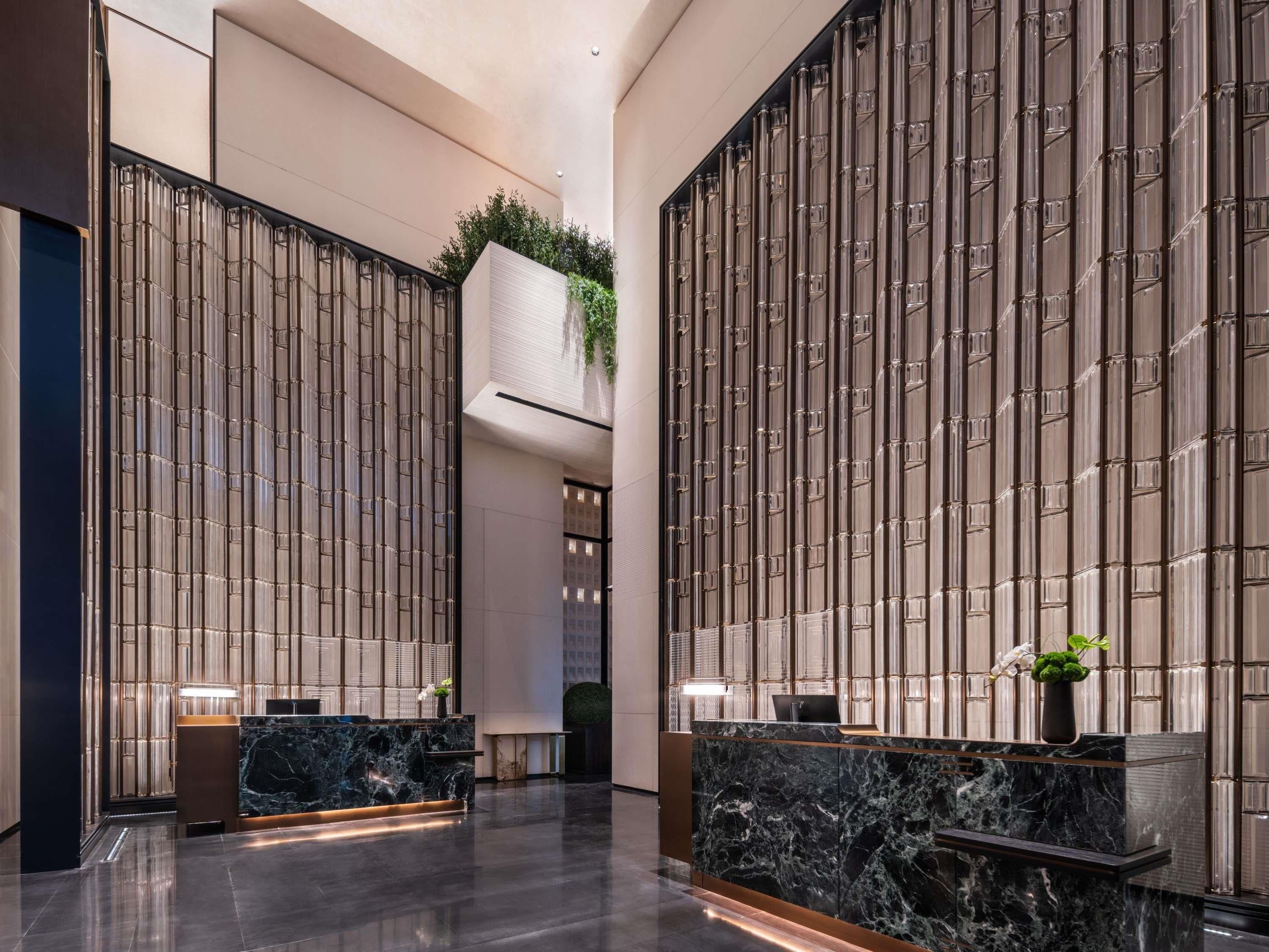 A modern lobby with a reception desk, vertical glass panels, and a central green plant.