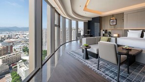 A modern hotel room with a curved ceiling, large windows offering a city view, a sofa, a dining table, and a bed. - Pullman Quanzhou Shuitou (Quanzhou)