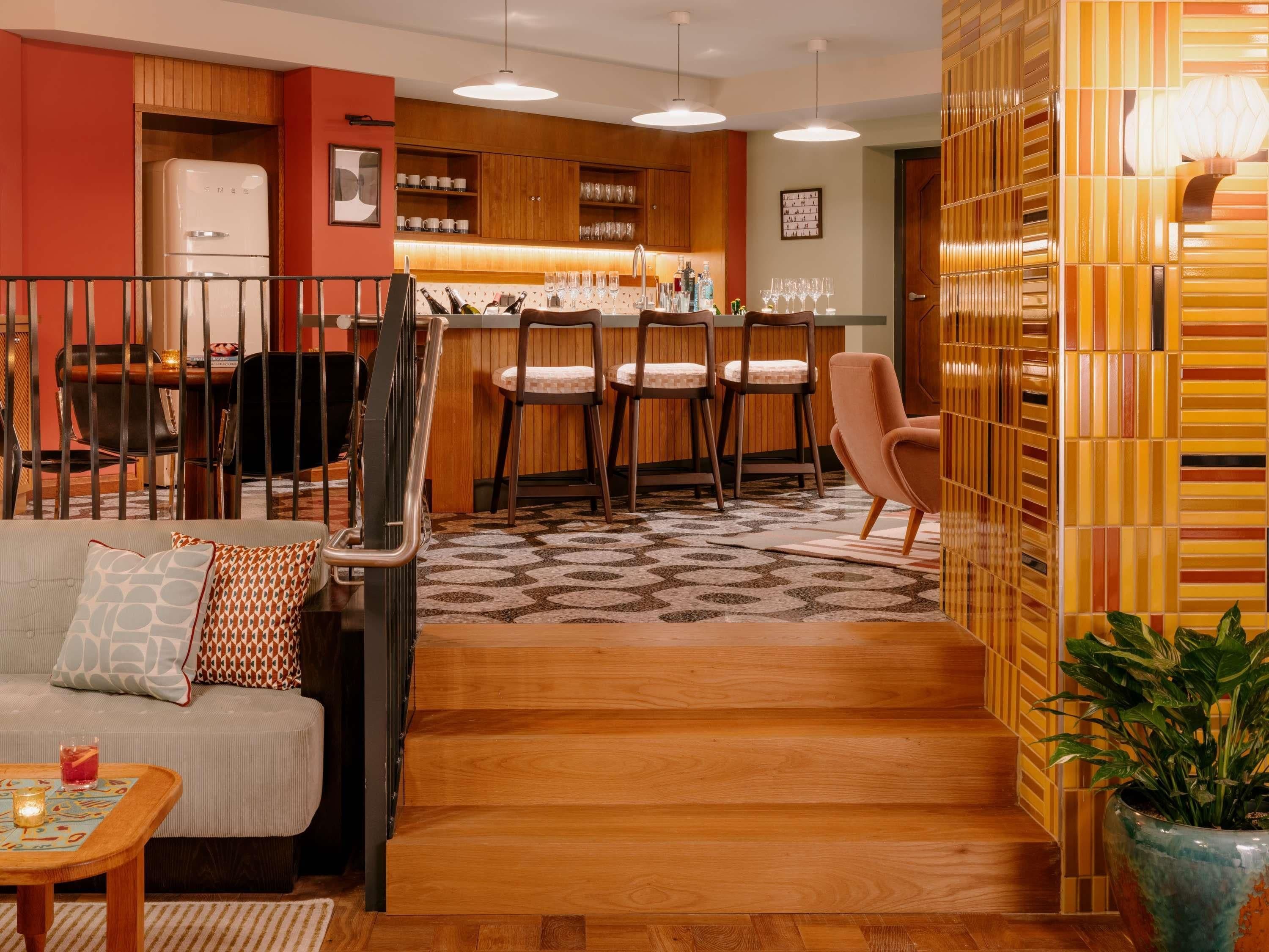 A modern kitchen with wooden cabinets, a dining area with chairs, and a staircase leading to another level.