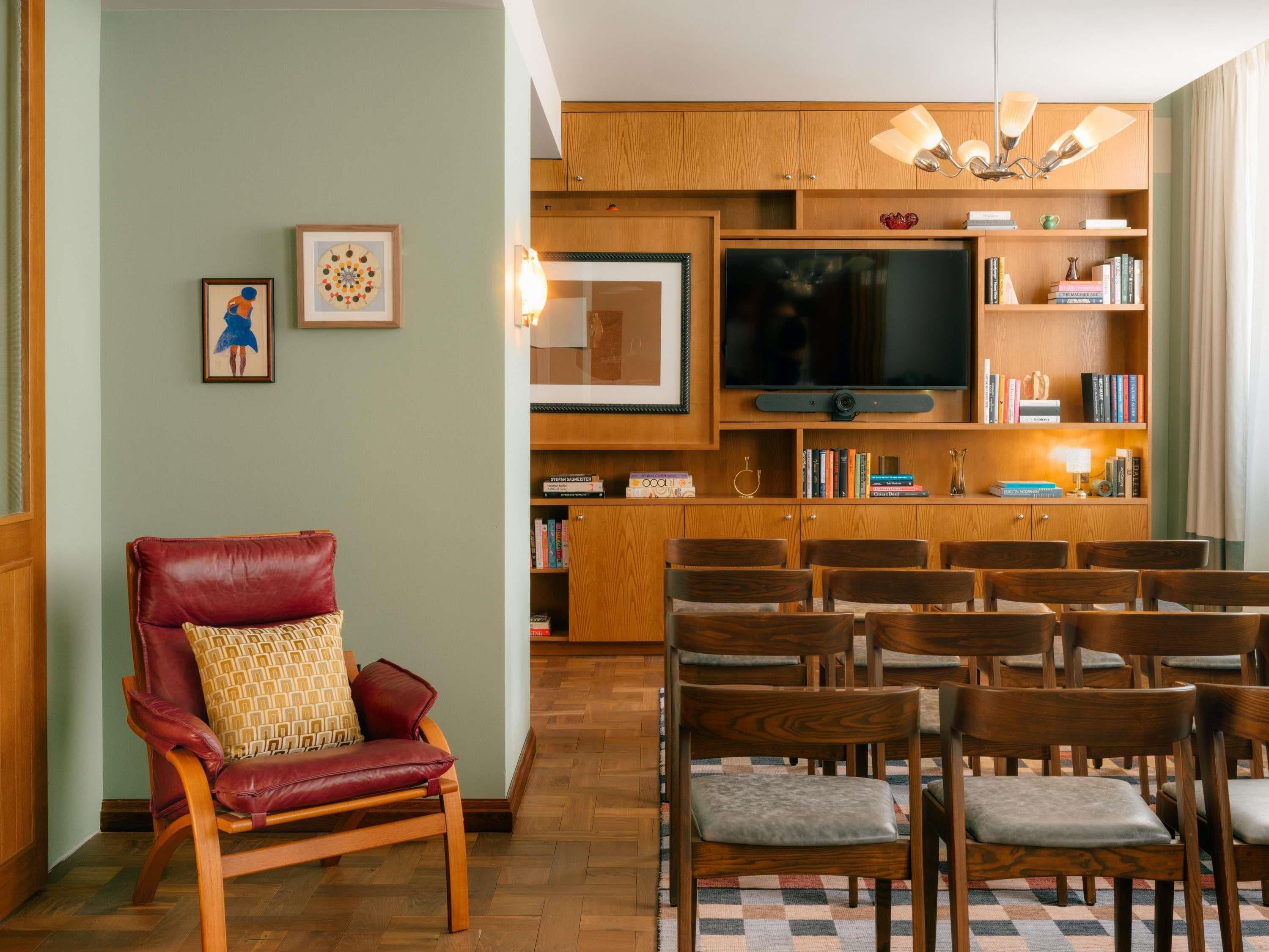 A living room with a red leather chair, wooden chairs, a television, bookshelves, and a patterned rug.
