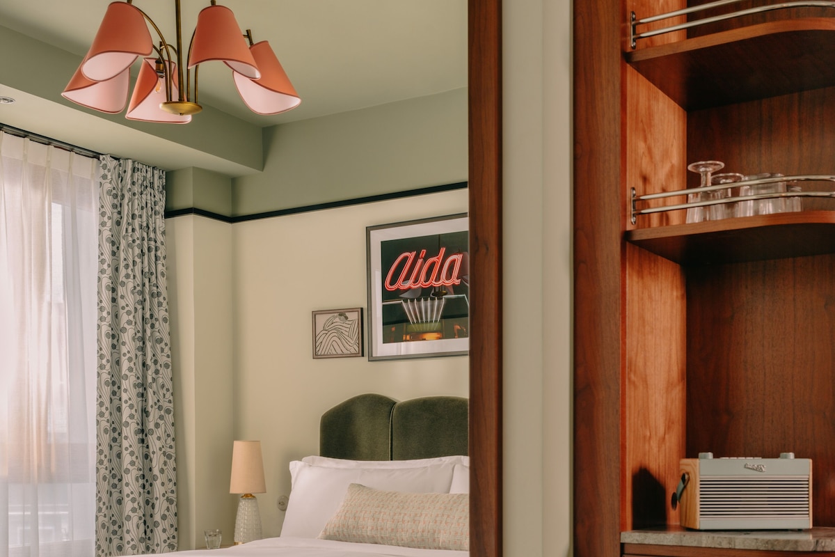 Une chambre à coucher bien rangée, avec un lit, une table de chevet, une lampe et une armoire en bois contenant de la verrerie.
