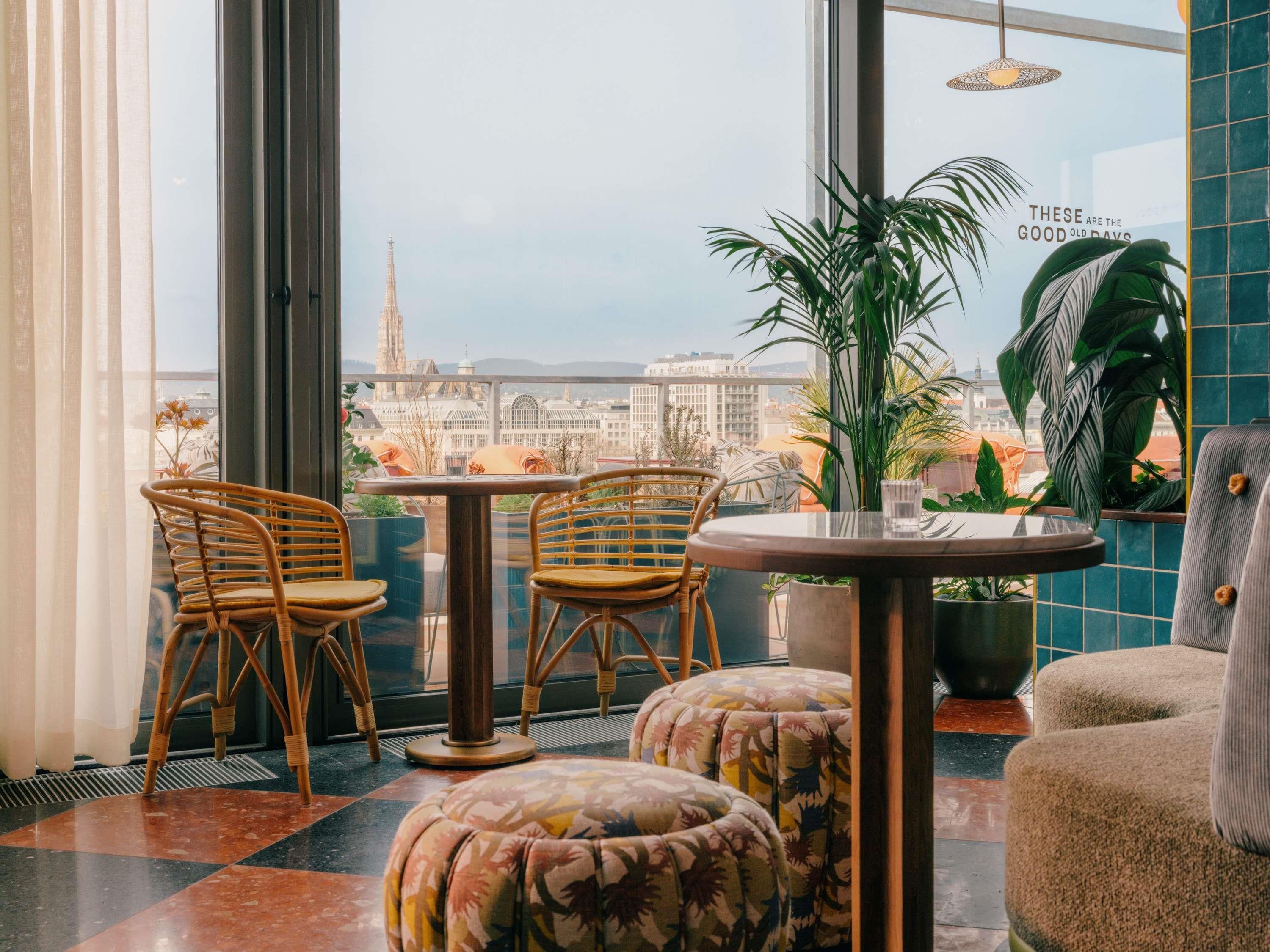 Ein modernes Interieur mit Korbstühlen, einem runden Tisch und Blick auf eine Stadtlandschaft durch große Fenster.