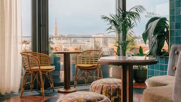 Ein modernes Interieur mit Korbstühlen, einem runden Tisch und Blick auf eine Stadtlandschaft durch große Fenster.