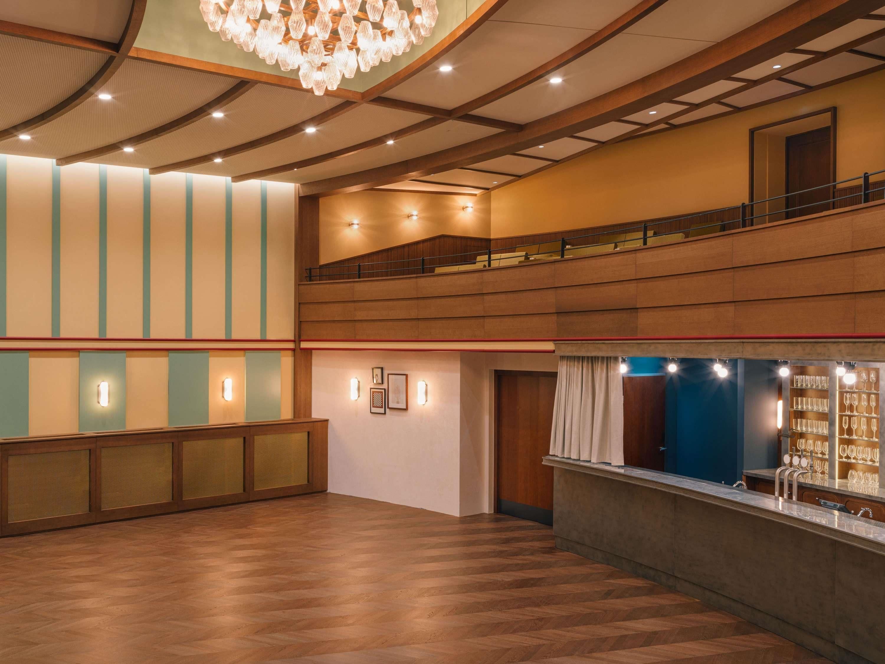 A spacious lobby with a wooden floor, a chandelier, a reception desk, and a glass display case with items.