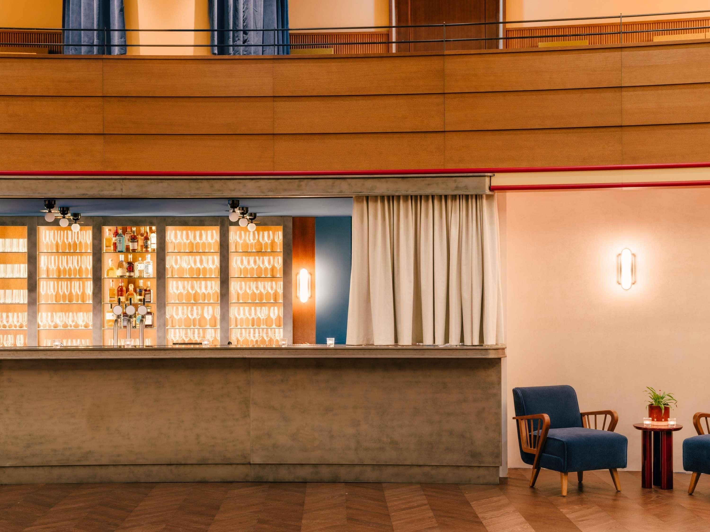A bar area with a counter, shelves of glasses and bottles, and a seating area with two chairs and a small table.