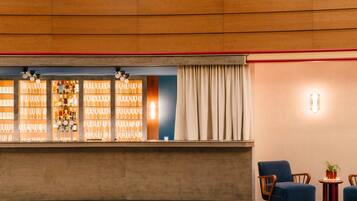 A bar area with a counter, shelves of glasses and bottles, and a seating area with two chairs and a small table.