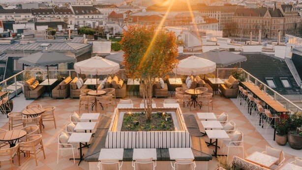 A rooftop terrace with outdoor seating, a central planter, and a view of the cityscape.