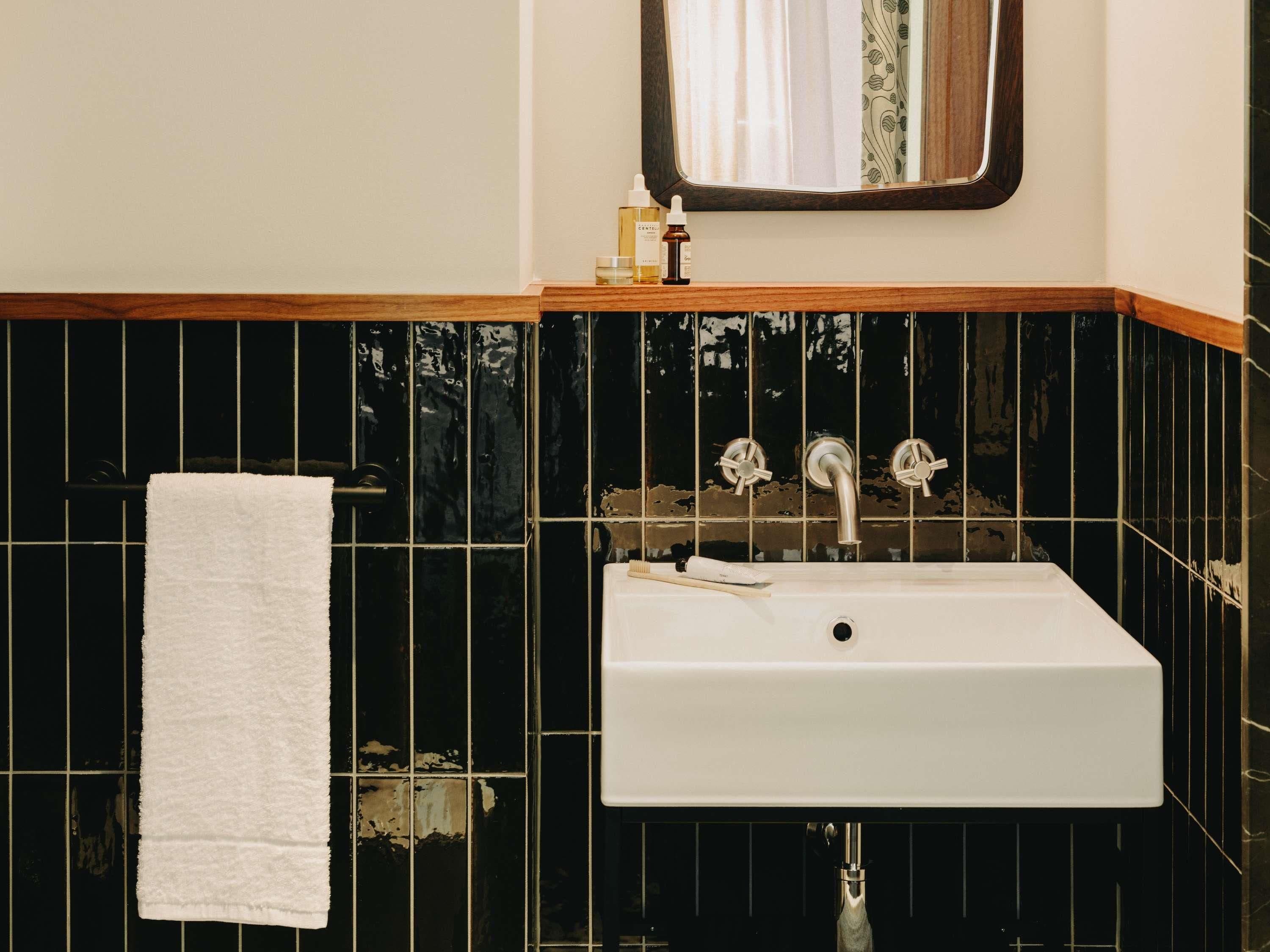 A bathroom with a white sink, black tiled walls, a white towel on a rack, and a mirror above the sink.