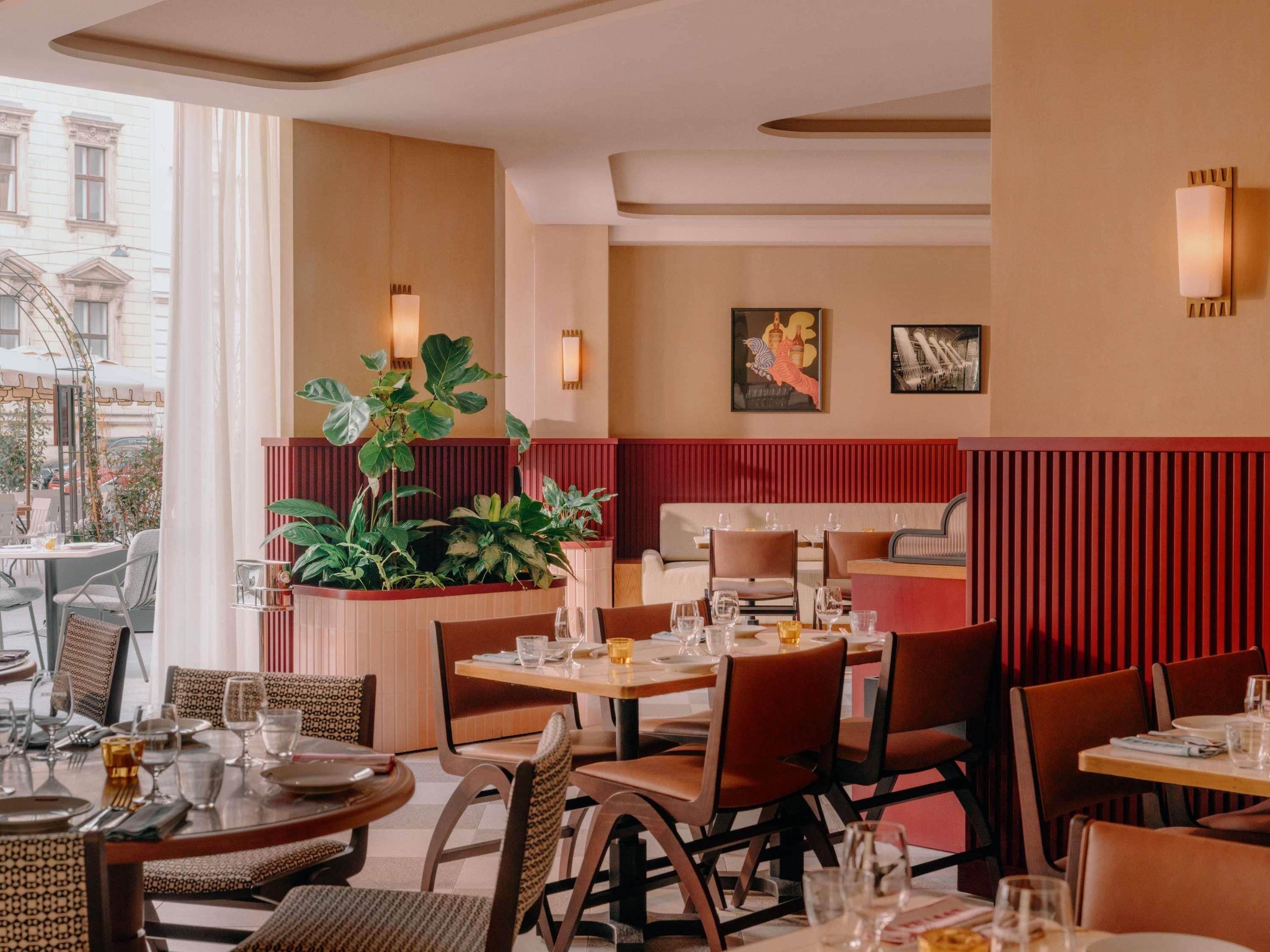 A restaurant interior with tables set for dining, a large potted plant, and artwork on the walls.