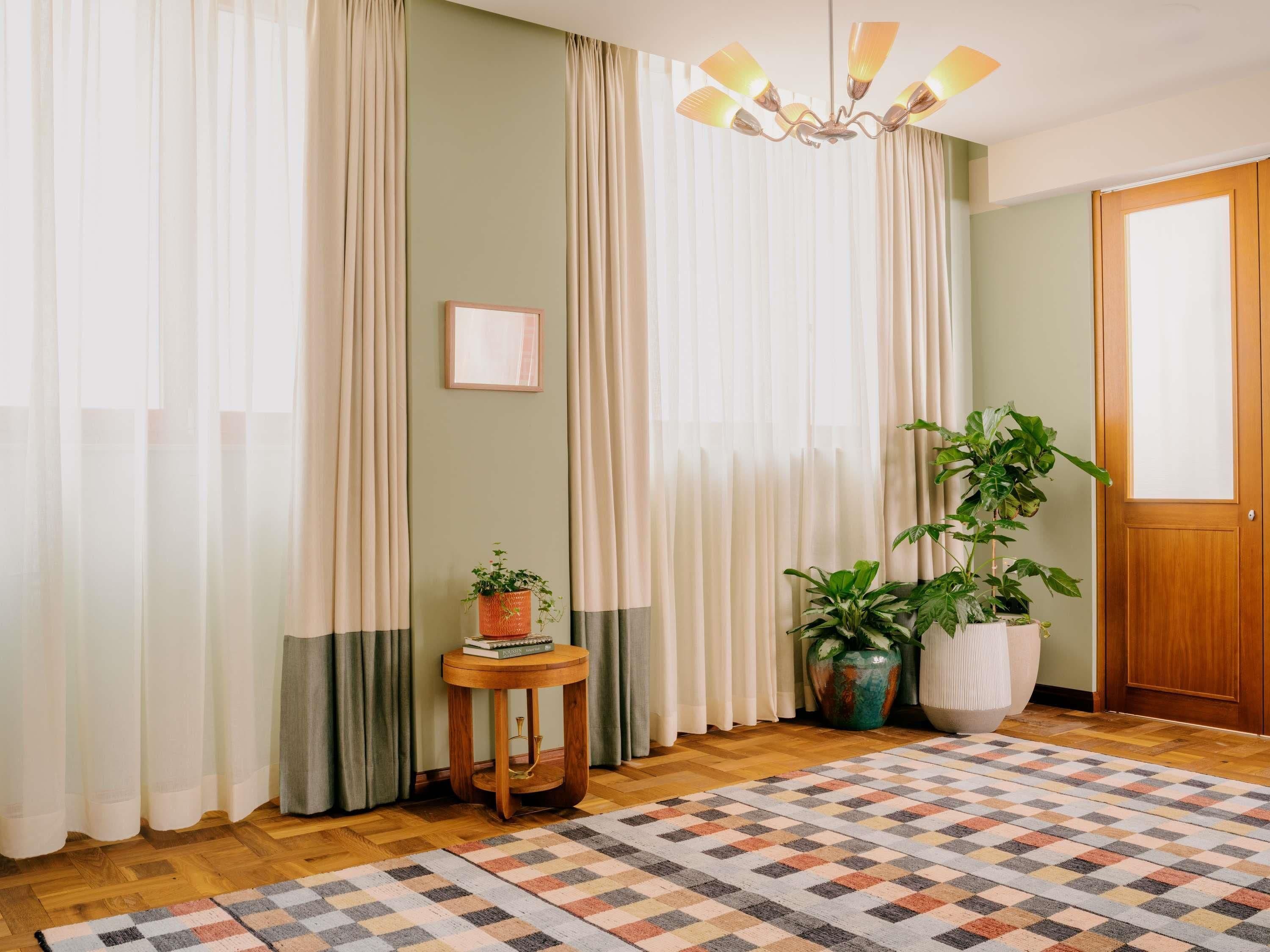Una habitación con un tapete estampado, una mesita de madera con una planta y una puerta con panel de madera.