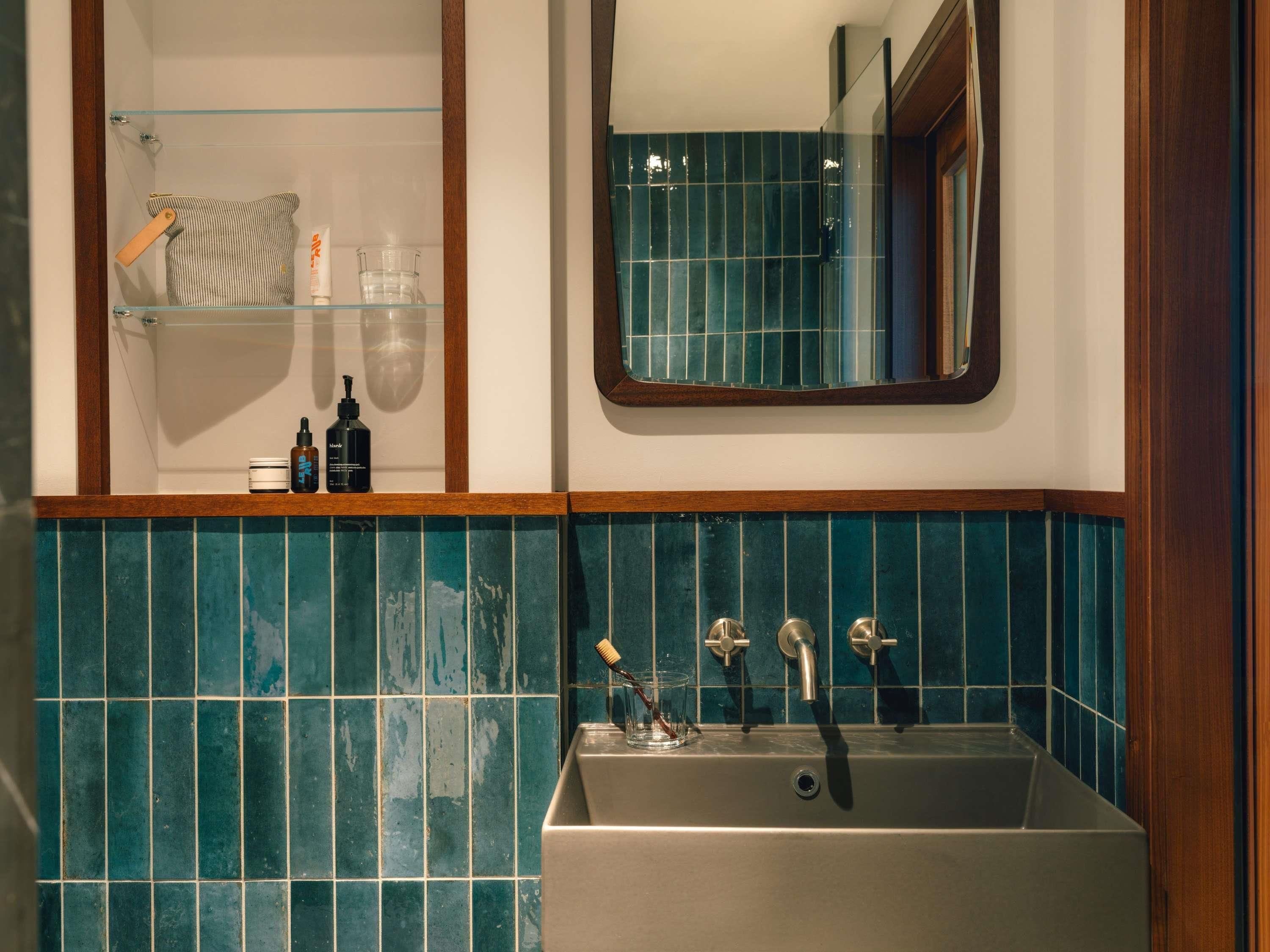 Casa de banho com lavatório, espelho e prateleiras com produtos de higiene pessoal.