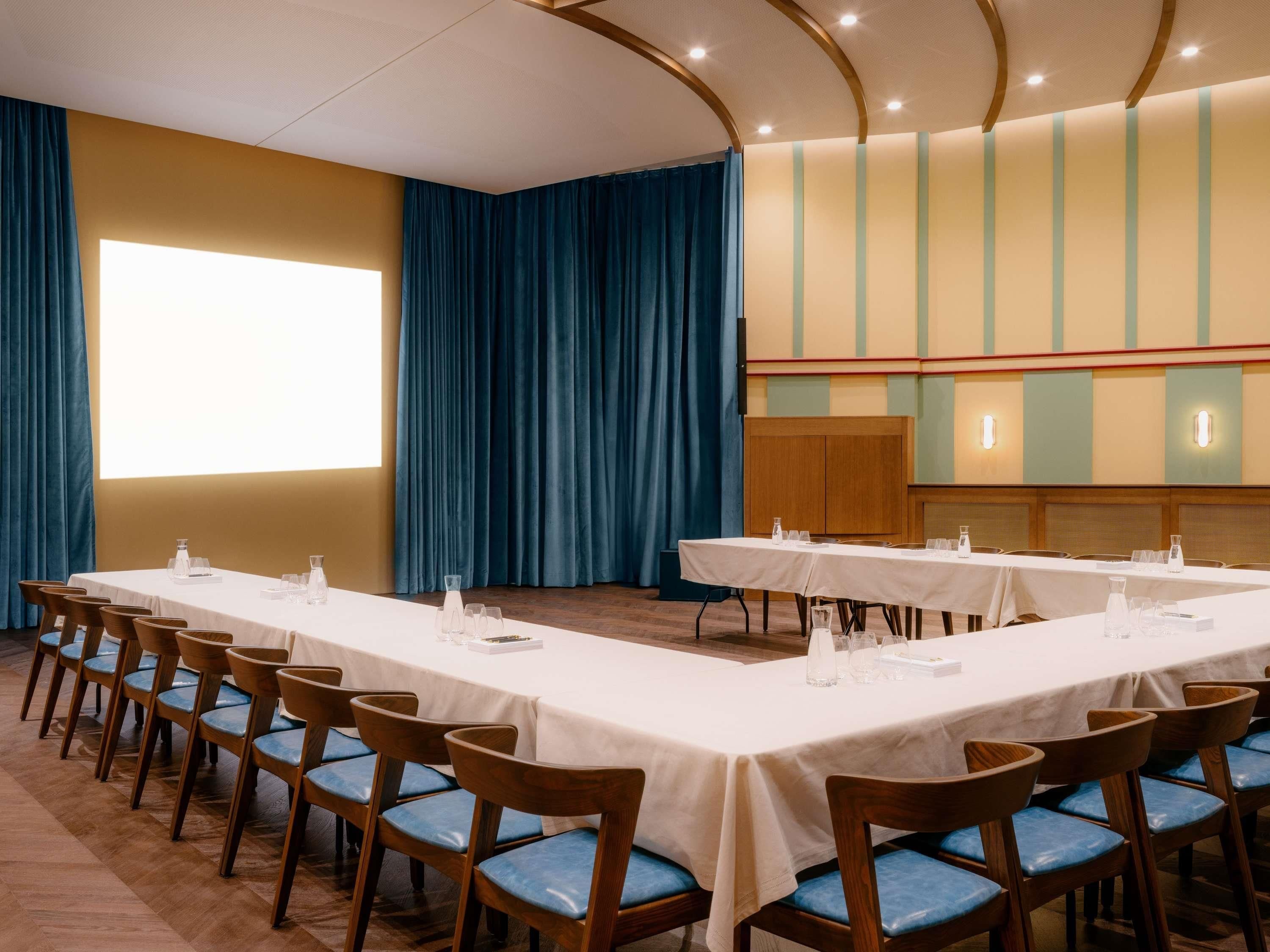 A conference room with long tables, chairs, and a large screen.