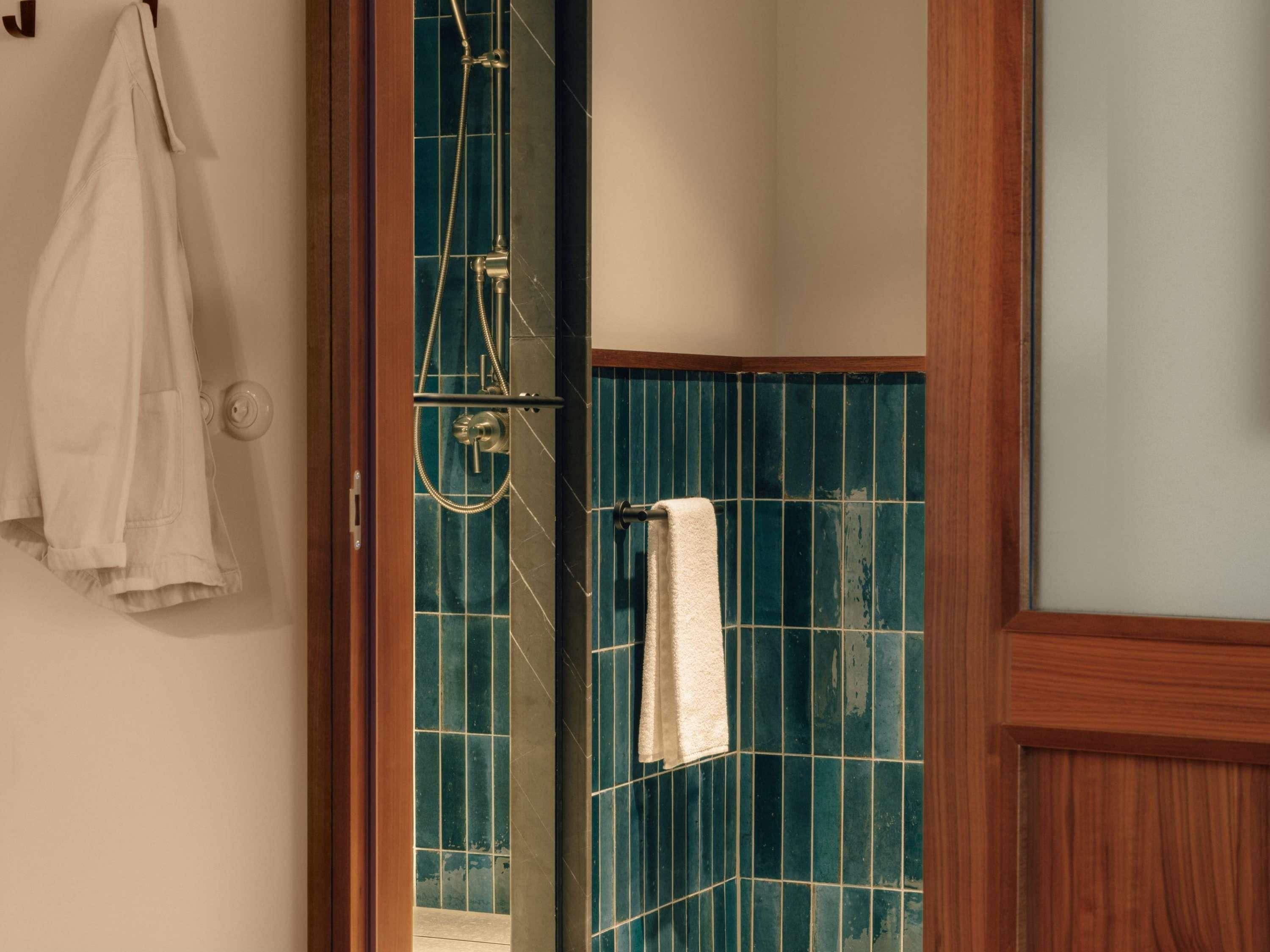 A bathroom with a shower, a towel hanging on the wall, and a wooden door frame.