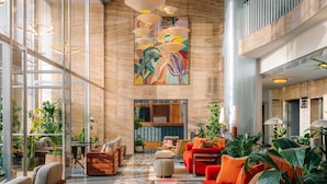 A spacious lobby with a high ceiling, a large abstract painting, and a variety of seating arrangements including sofas and armchairs.