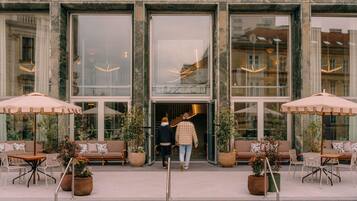 A hotel entrance with a glass facade, outdoor seating, and potted plants.