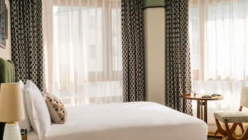 Quarto de hotel com cama, mesa redonda, cadeira e cortinas.