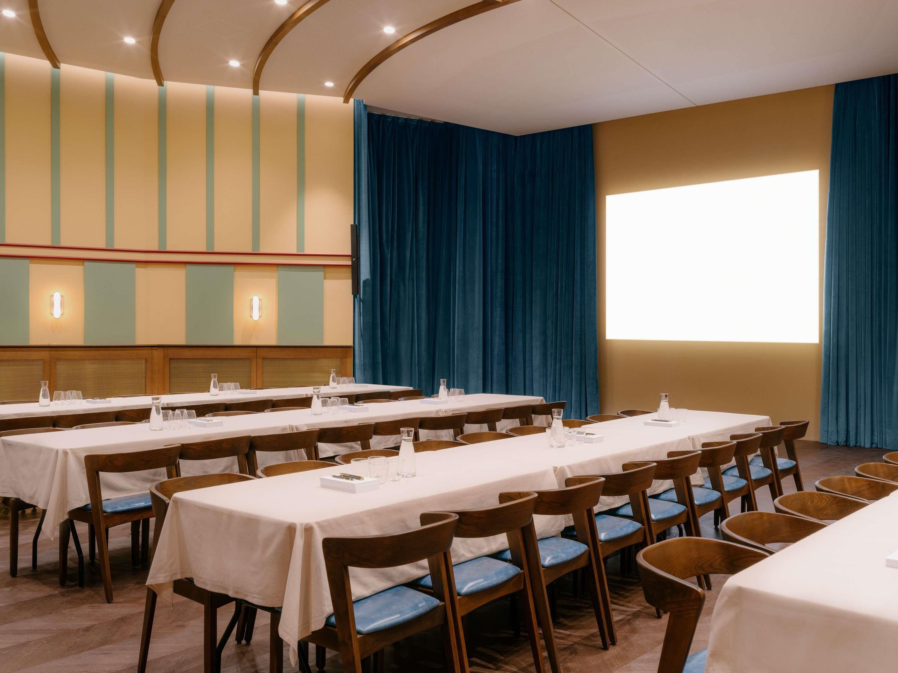 A conference room with multiple tables and chairs, a large window with curtains, and a ceiling with recessed lighting.