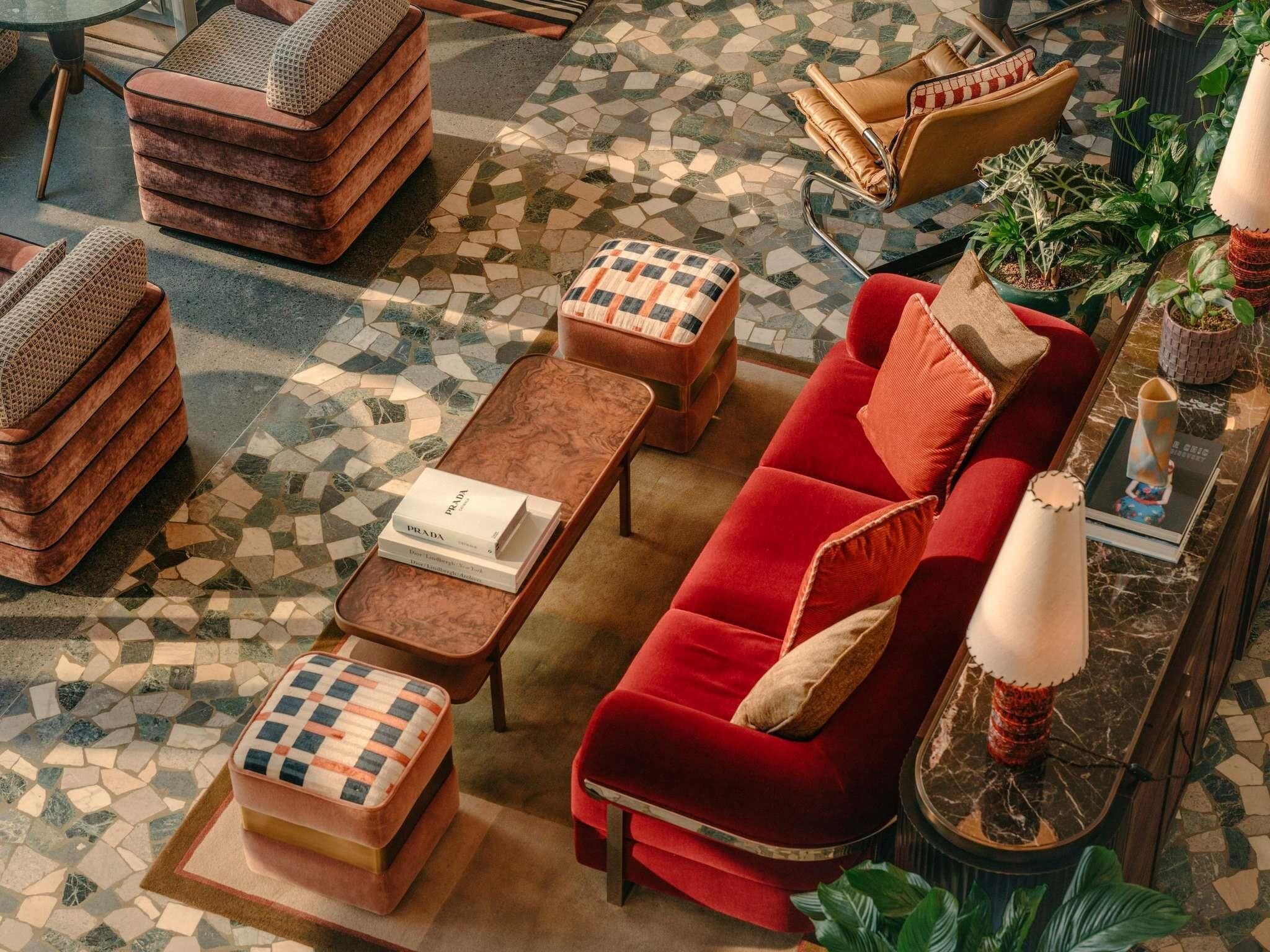 Uma sala de estar moderna com um sofá vermelho, pufes de madeira, uma mesa de centro e um piso estampado.