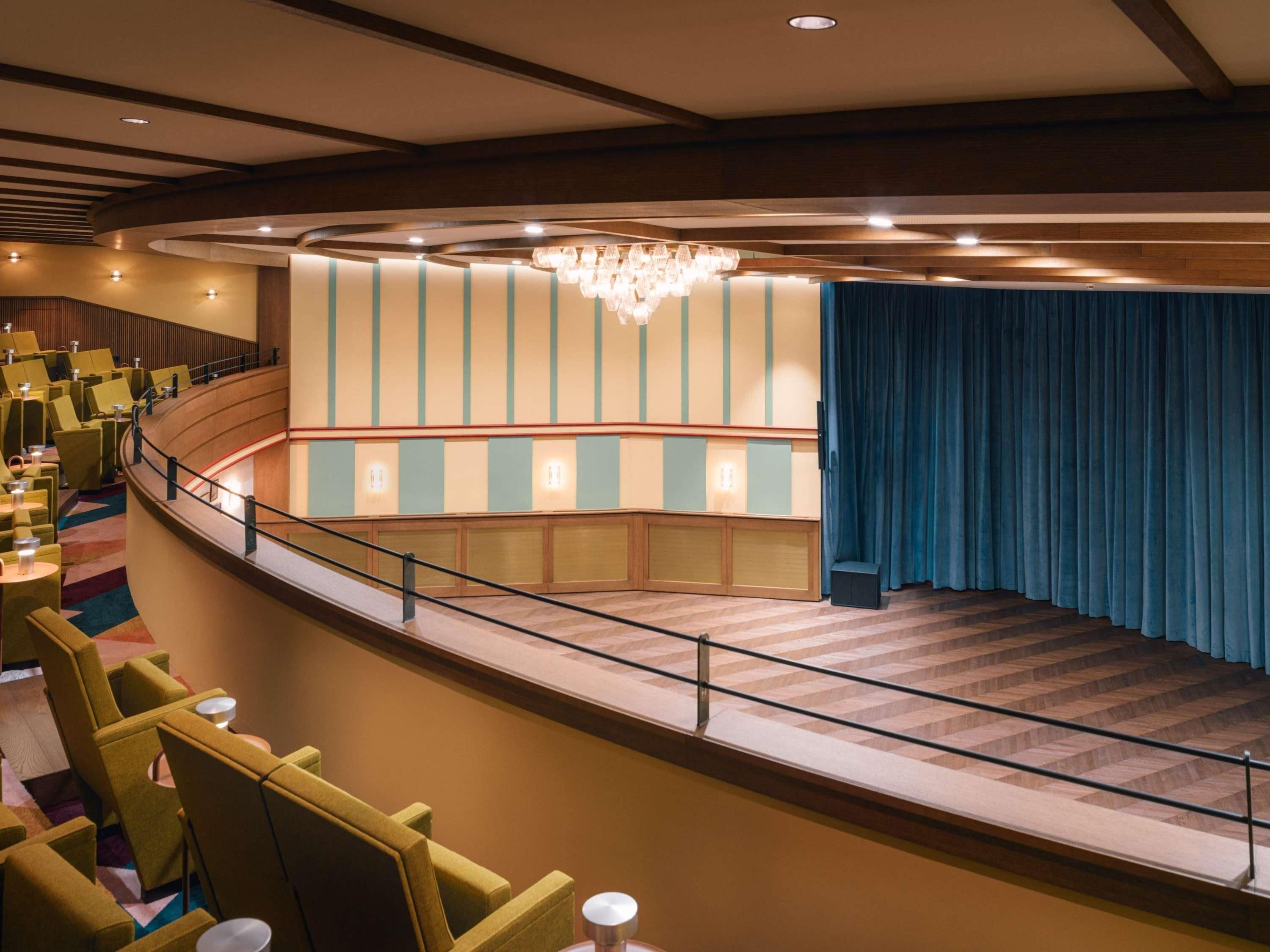 Un teatro con butacas escalonadas, un escenario y una araña.
