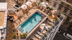 An aerial view of a rooftop pool area with lounge chairs and umbrellas, surrounded by buildings. - The Hoxton, Vienna (Vienna)