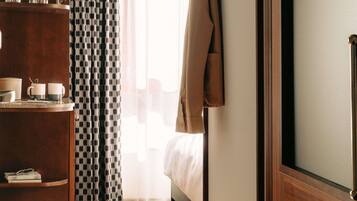 Habitación de hotel con una cama, un armario de madera, un estante con tazas y un libro, y una cortina estampada.