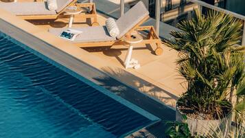 Ein Pool im Freien mit Liegestühlen und einem Tisch, umgeben von Topfpflanzen und einem Gebäude im Hintergrund.