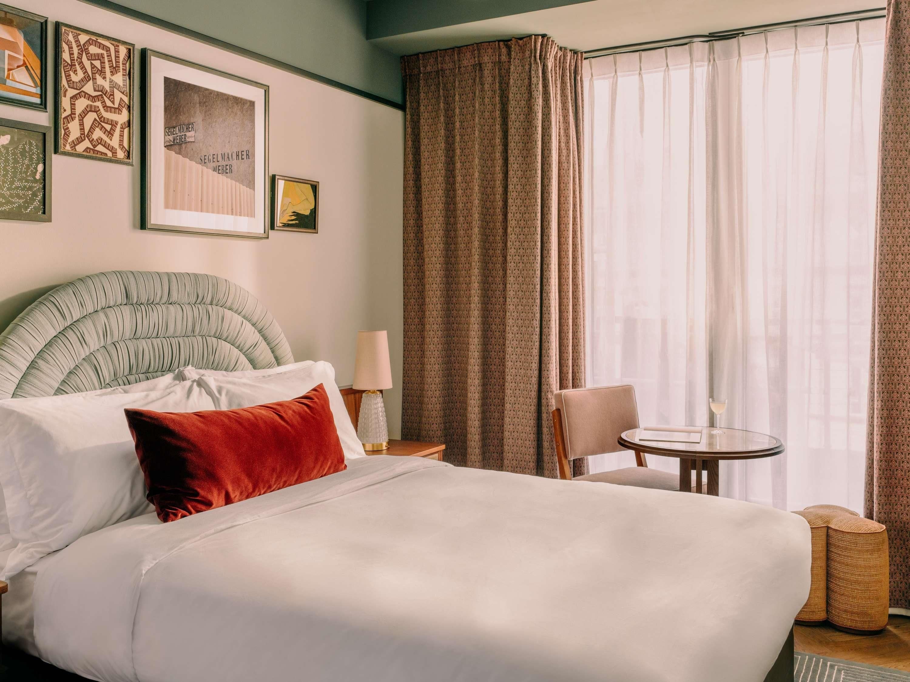 A hotel room with a large bed, a round table, a chair, and a window with curtains.