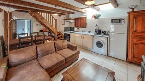 A cozy living room with a brown sofa and wooden coffee table, a kitchen with a washing machine, and a staircase leading to another level. - Amazing home in Asté with WiFi (Asté)