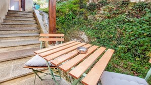 A wooden table with a metal ashtray, a bench, and a cushioned seat, set against a stone staircase and lush greenery. - Amazing home in Asté with WiFi (Asté)