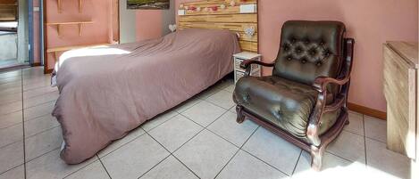 A bedroom with a bed, a leather armchair, a wooden headboard, a small bedside table, and a wall-mounted coat rack.