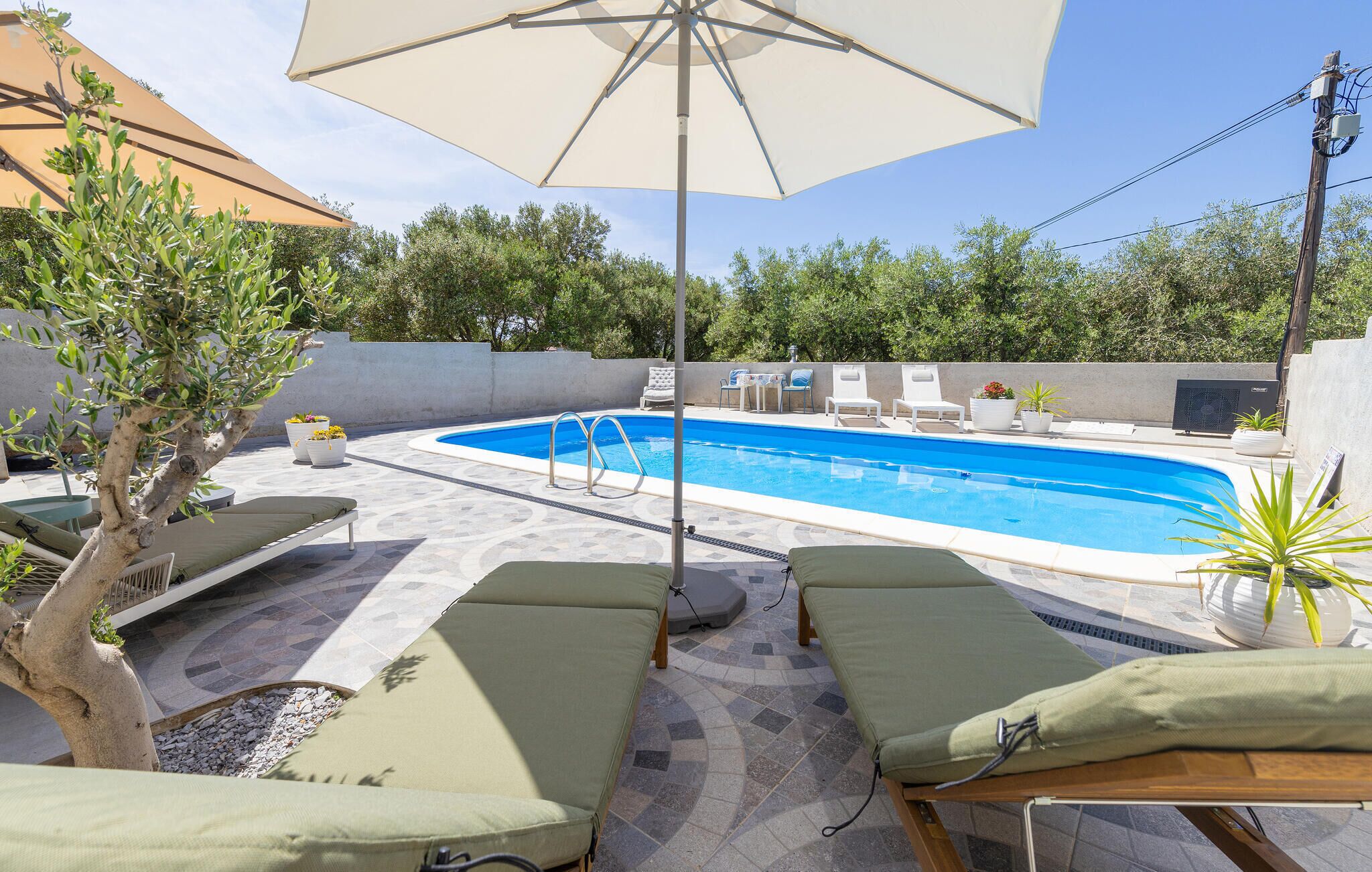 Ein Schwimmbecken mit Liegestühlen und Sonnenschirmen, umgeben von Bäumen und einer gefliesten Terrasse.