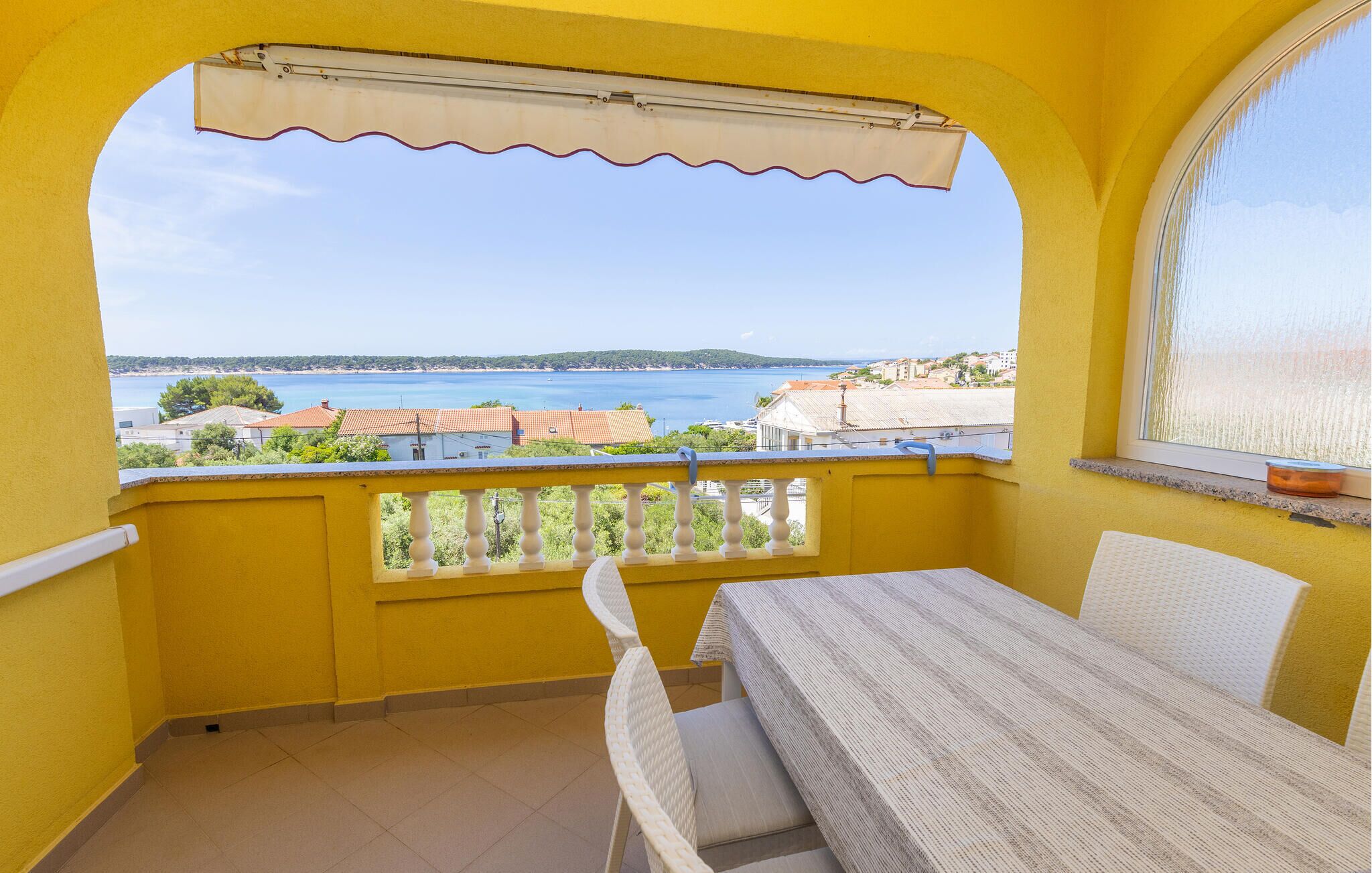 Ein Balkon mit Tisch und Stühlen und Blick aufs Meer, sowie eine gelbe Wand.
