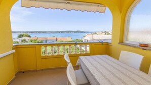 A balcony with a table and chairs, a view of the sea, and a yellow wall. - Nice apartment in Rab with heated swimming pool (Rab)