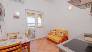A compact kitchen with a dining area, a sofa with cushions, and a view of the sea through a door. - Nice apartment in Rab with heated swimming pool (Rab)