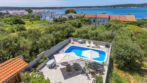 A rooftop pool with lounge chairs and umbrellas, surrounded by greenery and overlooking a coastal area. - Nice apartment in Rab with heated swimming pool (Rab)