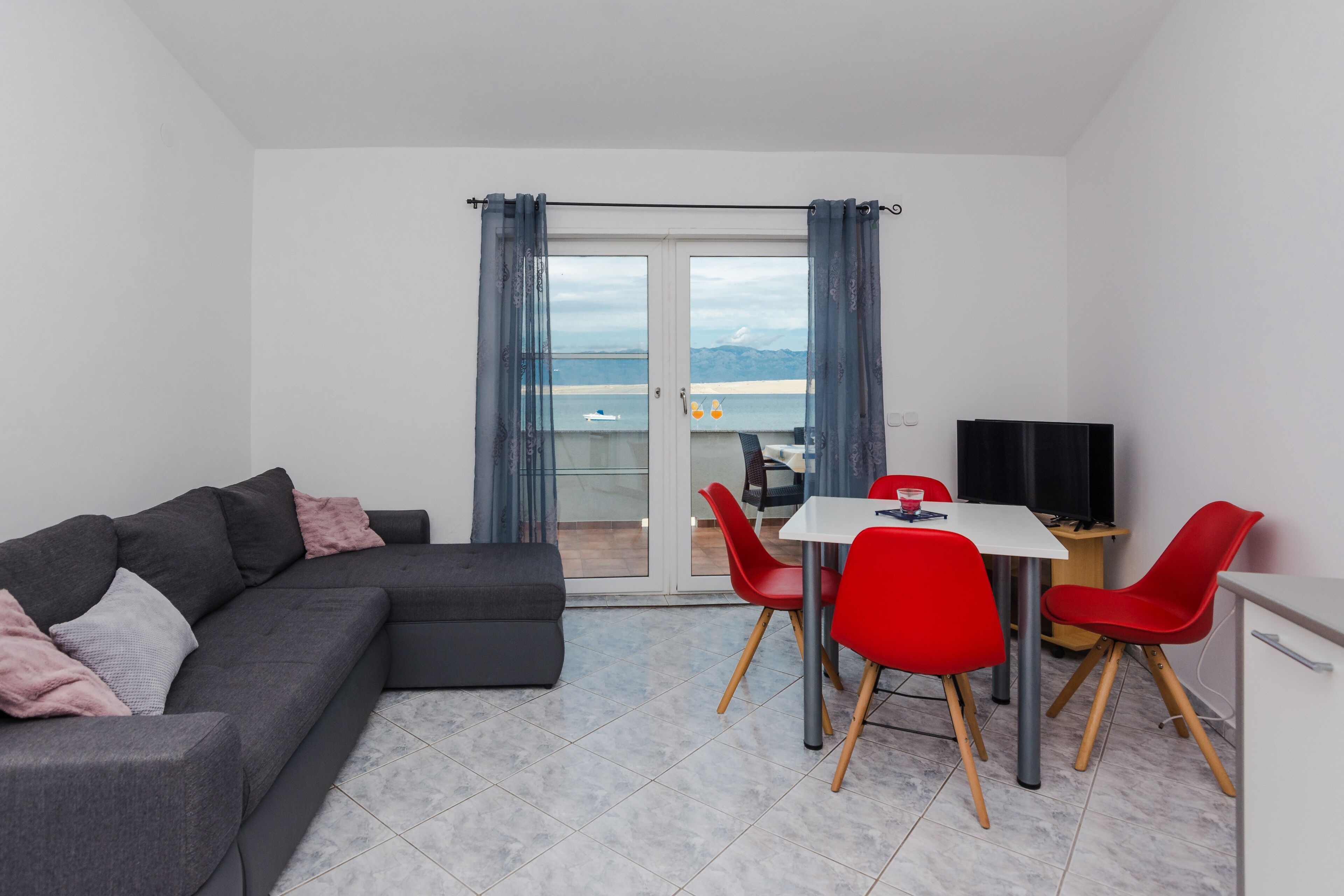Ein modernes Wohnzimmer mit grauem Sofa, roten Sesseln, einem weißen Tisch und einem Fernseher.