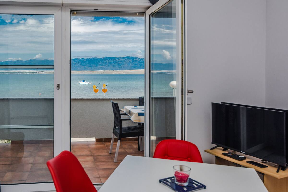 A room with a glass door leading to a balcony with a view of the sea and mountains.