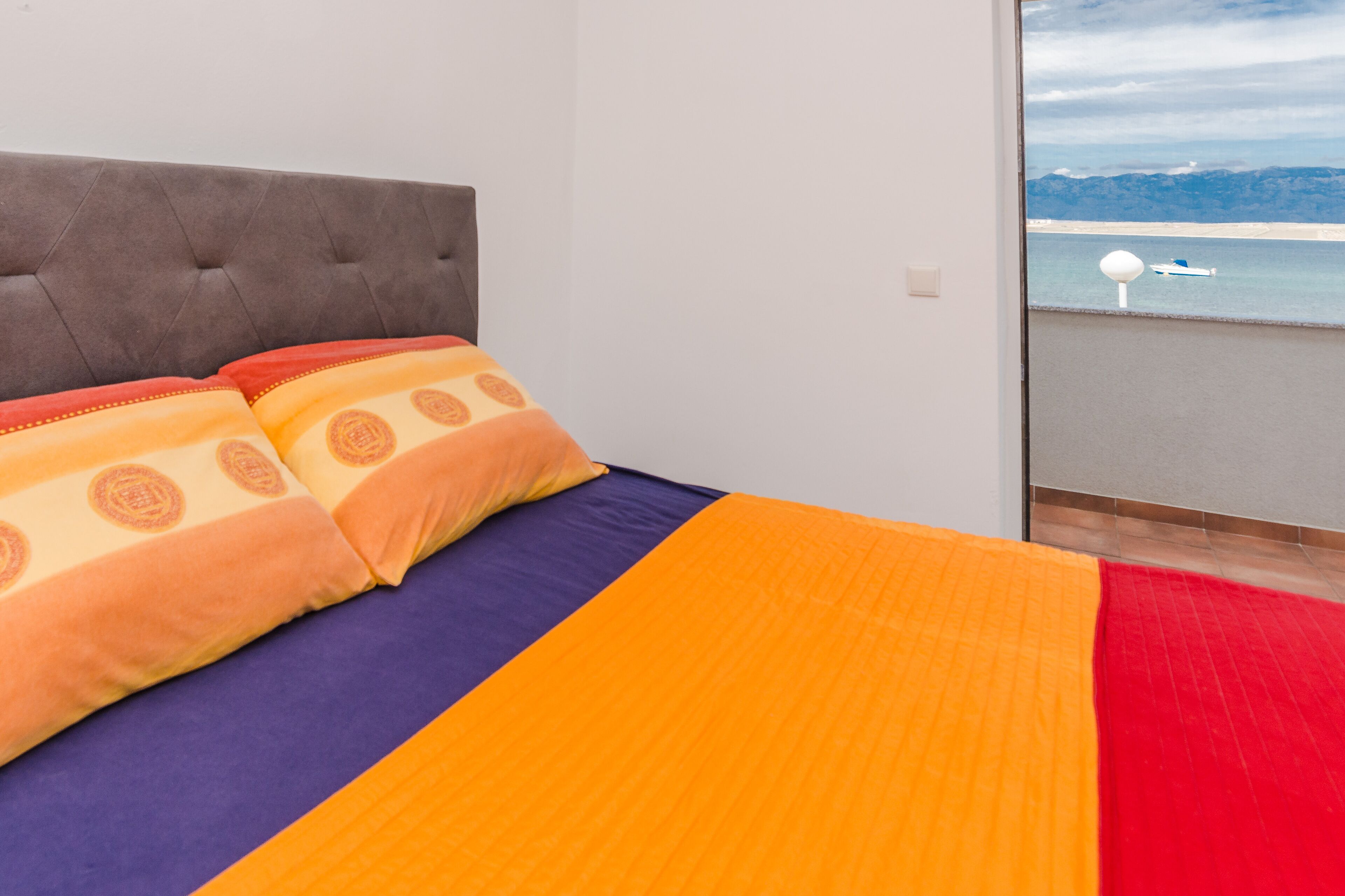 Ein Schlafzimmer mit Bett, Kissen und Meerblick durch ein Fenster.