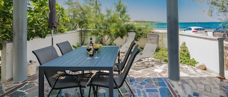 Eine Terrasse im Freien mit Tisch und Stühlen, einer Weinflasche und Blick aufs Meer.