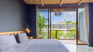 Un dormitorio con una cama grande, una mesita de noche, una lámpara colgante y vistas a un balcón con plantas y una valla.