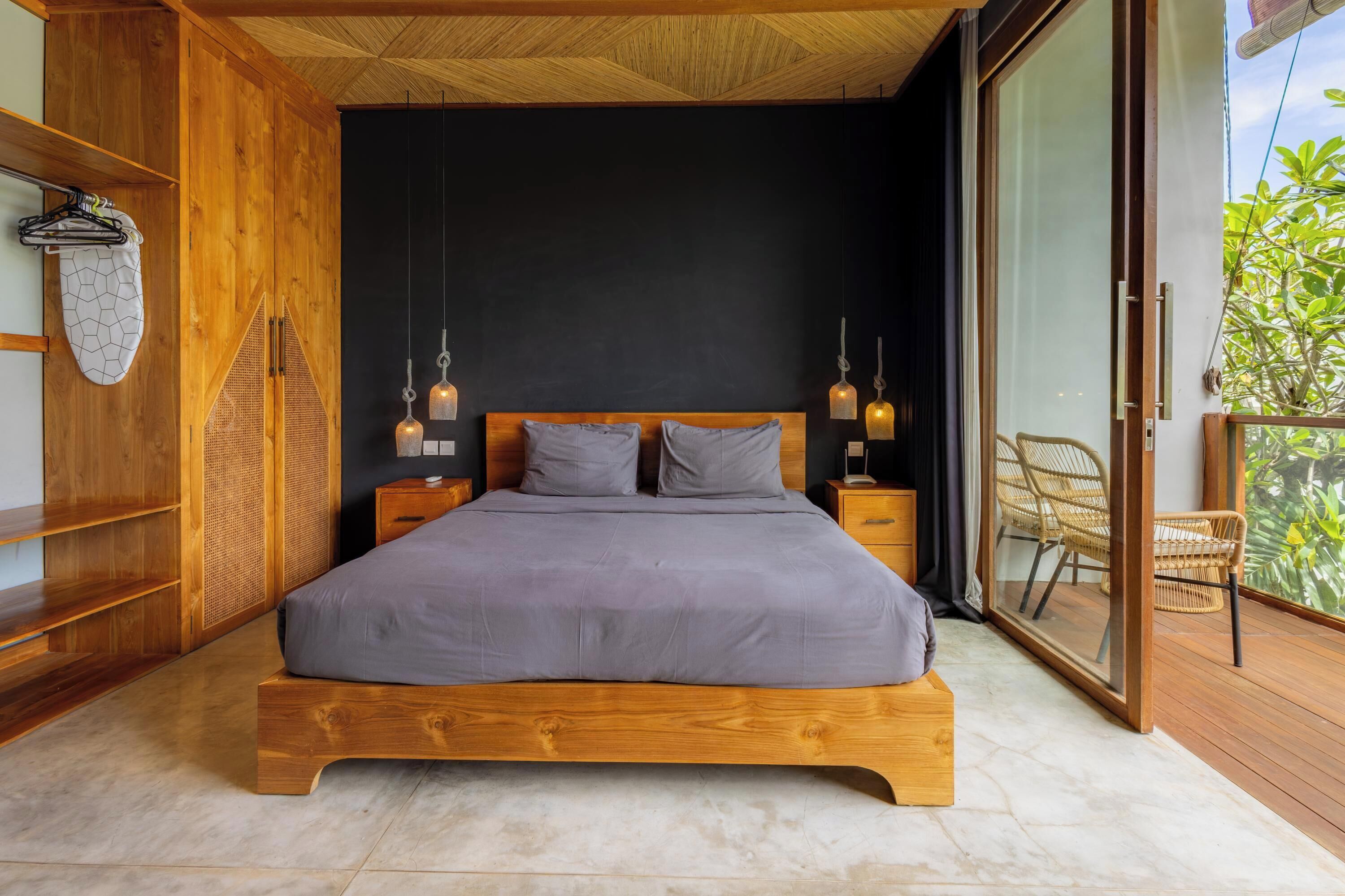 A bedroom with a wooden bed, two bedside tables, a large window, and a balcony with wicker chairs.