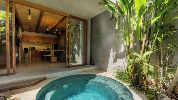 Una casa moderna con piscina, vigas de madera en el techo y una cocina visible a través de puertas de cristal.