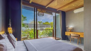 Un dormitorio con una cama grande, un escritorio y vistas a un balcón con vegetación.