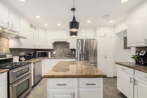 Eine moderne Küche mit weißen Schränken, Granit Arbeitsplatten, Edelstahlgeräten und einer schwarzen Pendelleuchte.