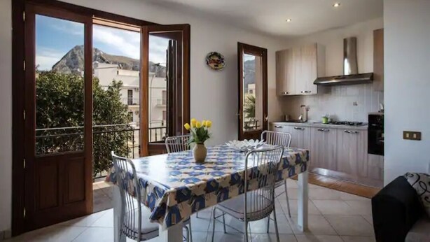 A dining area with a table set for four, a vase of yellow flowers, and a view of the outside balcony. - 🌞 ENJOY CASA MATTARELLA 🌞 San Vito lo Capo (San Vito Lo Capo)