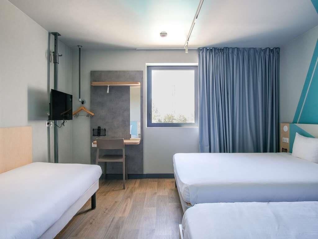 Une chambre d’hôtel avec deux lits, un bureau, une télévision et une fenêtre avec des rideaux.