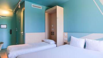 Habitación de hotel con dos camas, una puerta, una rejilla de ventilación y una lámpara fijada a la pared.
