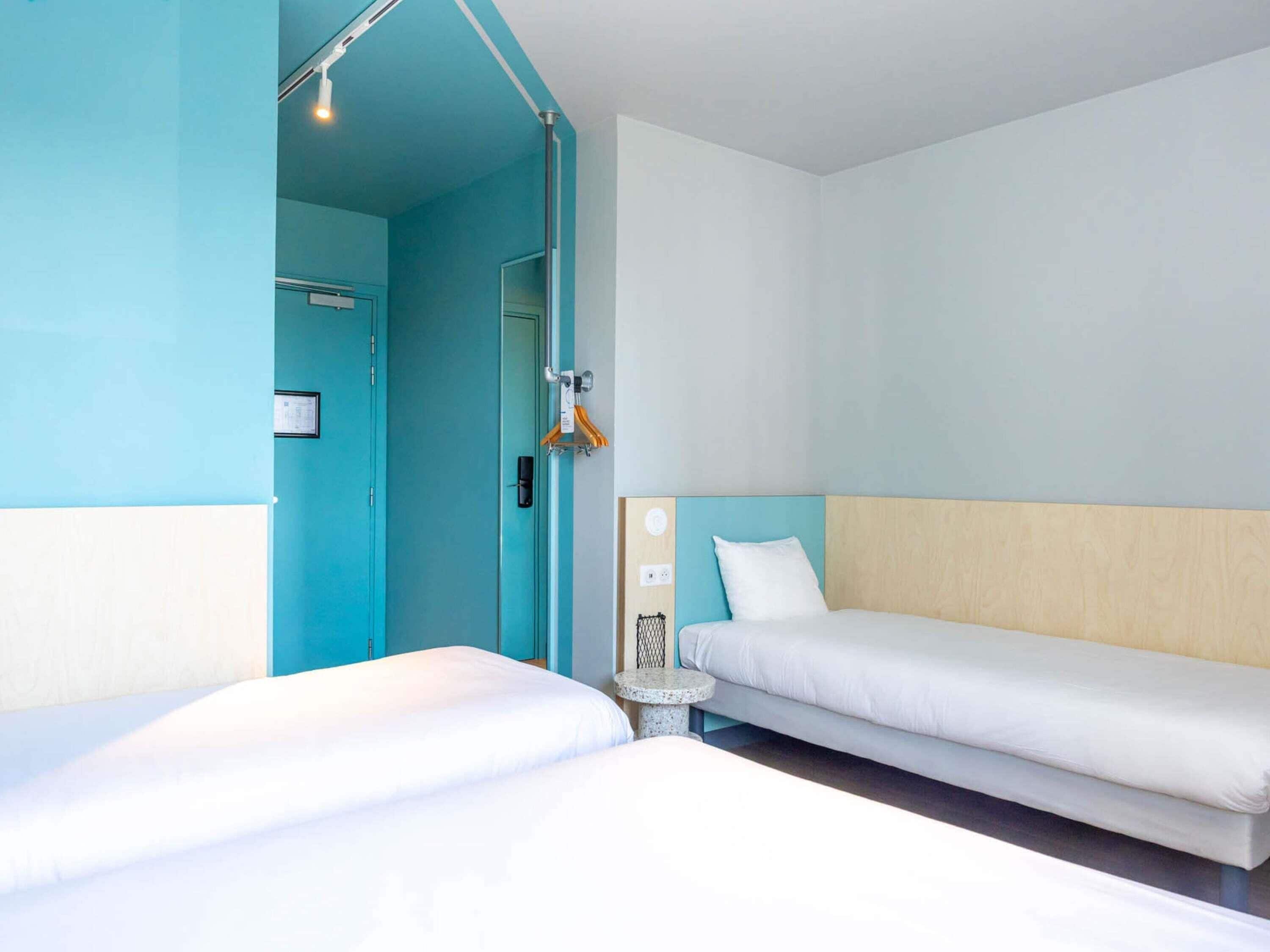 Een hotelkamer met twee bedden, een klein rond tafeltje en een deur naar een badkamer.
