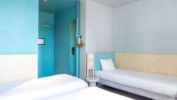 Een hotelkamer met twee bedden, een klein rond tafeltje en een deur naar een badkamer.