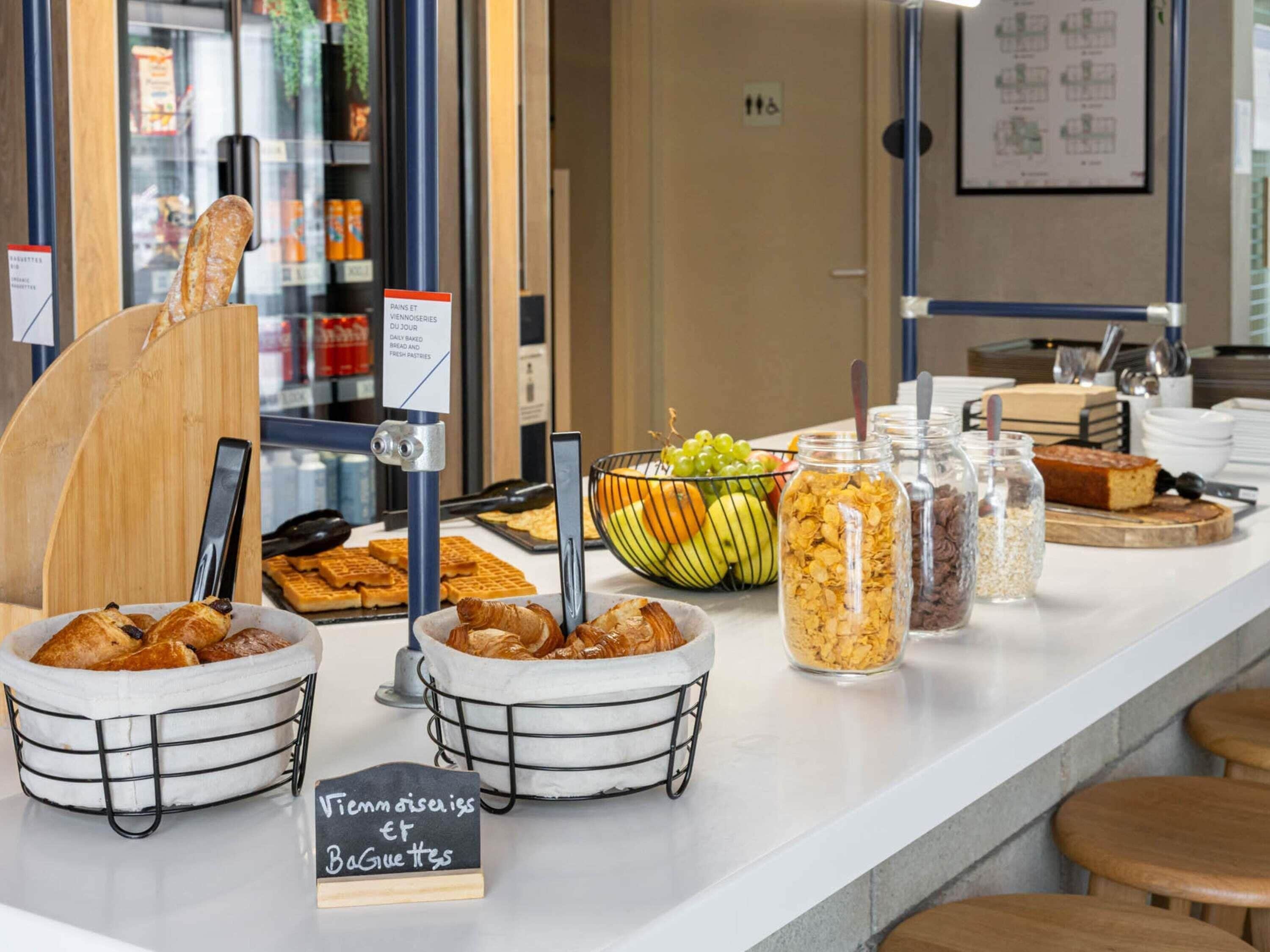 A breakfast buffet with bread, pastries, fruits, and cereals.